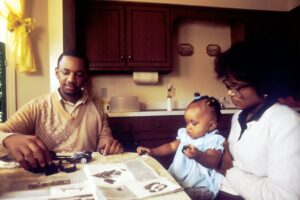 A family reviews health insurance documents, a calculator, and prescription bottles at a kitchen table.