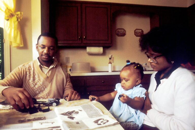 A family reviews health insurance documents, a calculator, and prescription bottles at a kitchen table.